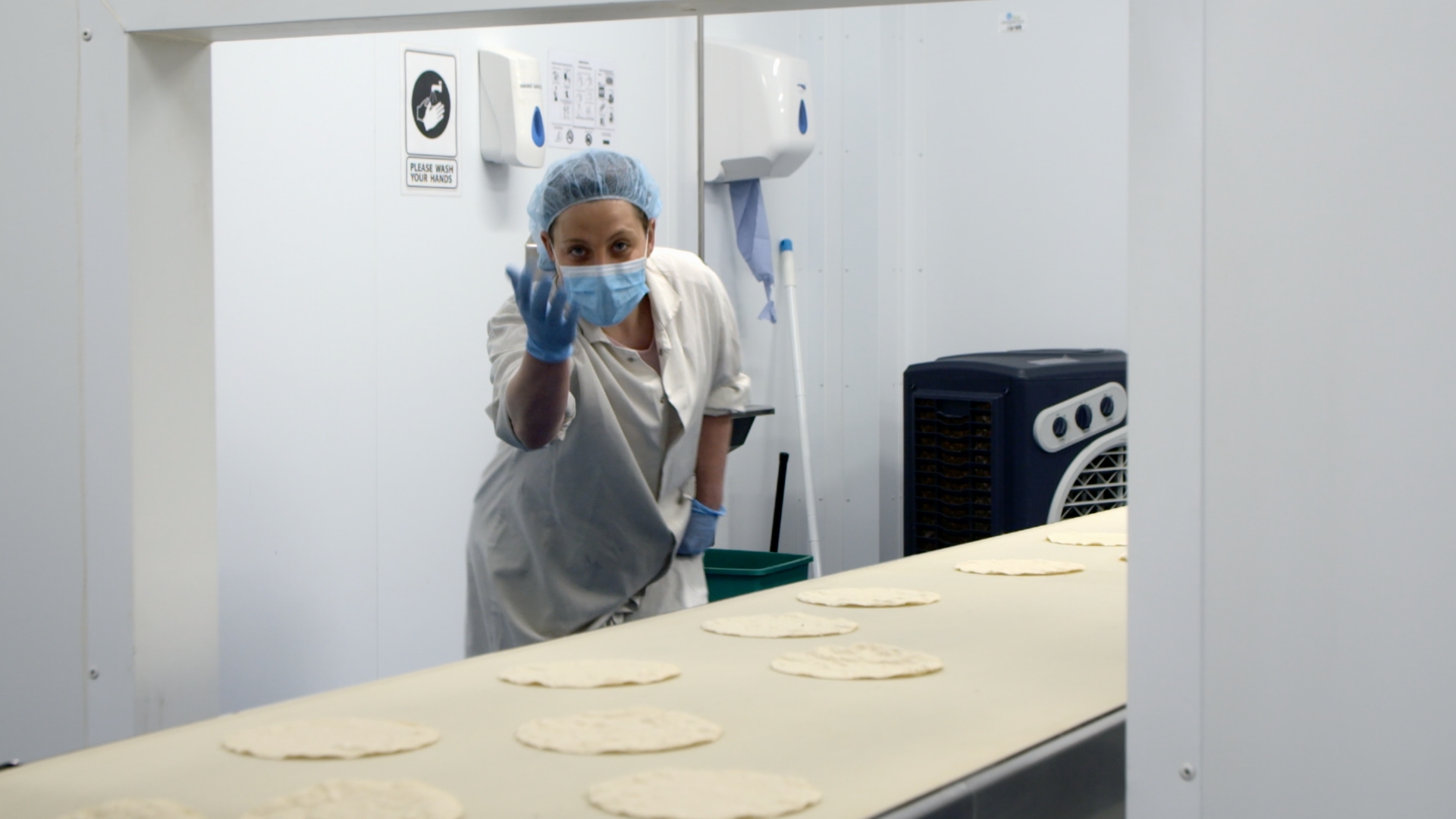 Person inside a factory, with tortillas in front of person.